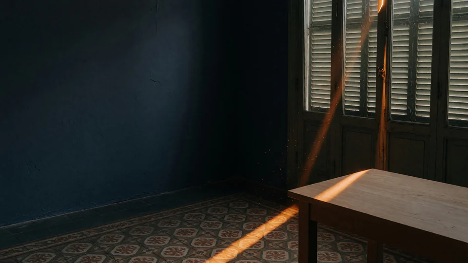 Estudio de ingeniería oscuro y minimalista al atardecer, con una fina línea de luz terracota que forma un bucle sobre un escritorio con un portátil y luz cálida entrando por ventanas altas.